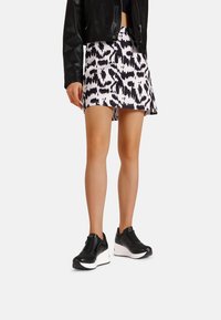 Giubbotto di pelle nera, gonna bianca con motivo astratto nero e sneakers sportive nere con suole bianche. Focus su stile casual e comfort.