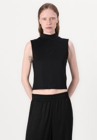 Black sleeveless crop top with a high neck. Soft, stretchy fabric. Features fitted design and smooth texture. Paired with black elastic-waist trousers.