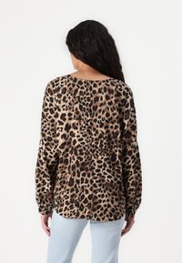 Langærmet bluse med leopardmønster, rund halsudskæring, i beige og sort farver, blød tekstur og afslappet pasform, båret med lyseblå jeans.