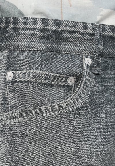 Grå denimstoff med en frontlomme med synlige sømmer og kontrasterende metallknappeaksenter. Teksturert med et falmet mønster.