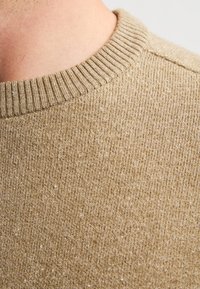 Beige gebreide trui met een ribbelboord bij de ronde hals, een textuurstof met een subtiel patroon en een zachte afwerking.