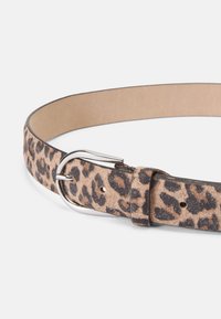 Opasok s leopardím vzorom vyrobený z semišu, s striebornou prackou a nastaviteľnými otvormi. Pozadie je neutrálne, aby zvýraznilo dizajn opasku.