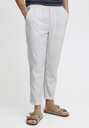 White cotton blend pants with an elastic waistband, side pockets, tapered fit, and smooth texture, paired with brown sandals.