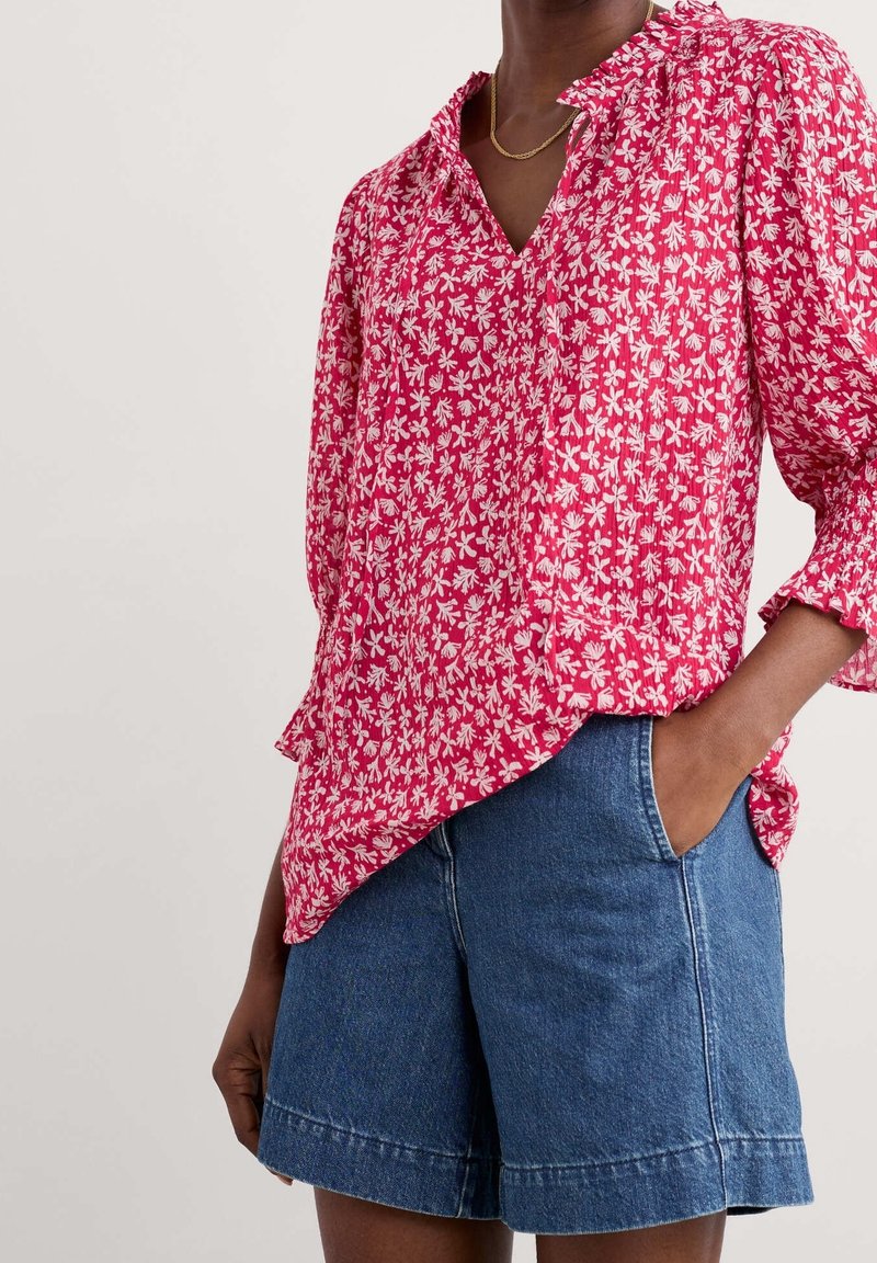 Rød blomstertrykt skjorte med V-hals, lange ærmer og en let asymmetrisk kant. Bæres sammen med denimshorts med sidelommer.
