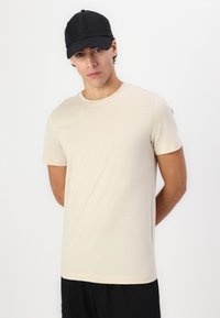 Bežs īsām piedurknēm krekls, kas izgatavots no mīksta auduma ar apaļu kakla izgriezumu. Tam pievienots melns cepures, ar strukturētu dizainu.