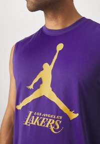 Homme portant un débardeur violet avec une silhouette jaune d'un joueur de basket-ball et un texte "Los Angeles Lakers".