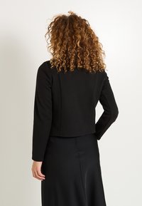 Chaqueta corta negra de tejido suave con mangas largas; presenta un diseño limpio y sencillo y una superficie lisa y sin adornos.