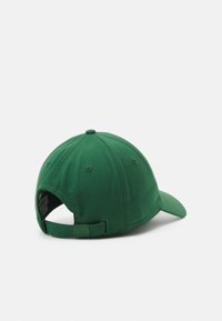 Grønn cap med buet skygge, laget av stoff. Har et justerbart stropp bak og en rund topp med ventilasjonsHull.