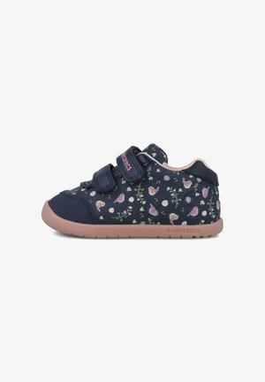 Zapatilla azul marino con patrón floral y pájaros, con dos correas de velcro y suela de goma rosa, fabricada con materiales textiles y sintéticos.