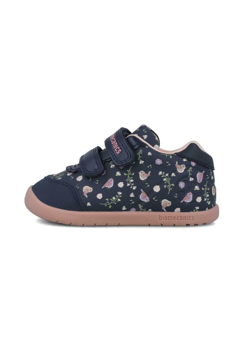 Zapatilla azul marino con patrón floral y pájaros, con dos correas de velcro y suela de goma rosa, fabricada con materiales textiles y sintéticos.