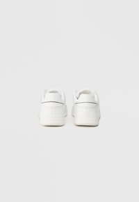 Ζευγάρι λευκών χαμηλών αθλητικών παπουτσιών που παρουσιάζονται από πίσω σε απλή ανοιχτό γκρι φόντο.