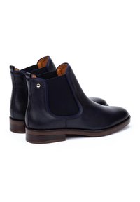 Bottes Chelsea en cuir marine avec panneaux latéraux élastiques, semelle marron et accent doré sur le talon. Texture lisse et design à bout arrondi.