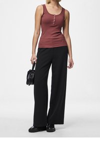 Canotta a coste bordeaux con cinque bottoni sul davanti, abbinata a pantaloni neri a gamba larga e una piccola borsa nera.