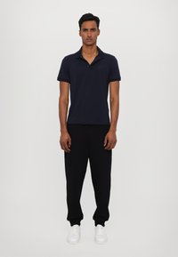Navy blue polo shirt with a subtle logo, paired with black sweatpants and white sneakers. The shirt features a soft texture and short sleeves.