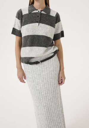 Kobieta ubrana w szaro-białą koszulkę polo w paski z krótkim rękawem, włożoną do jasnoszarej, prążkowanej spódnicy dzianinowej z czarnym paskiem.