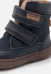 Navyblauwe kinderlaars met dubbele klittenbandsluitingen, gemaakt van leer en textiel, met een gestructureerde rubberen zool en tan accenten op de banden.
