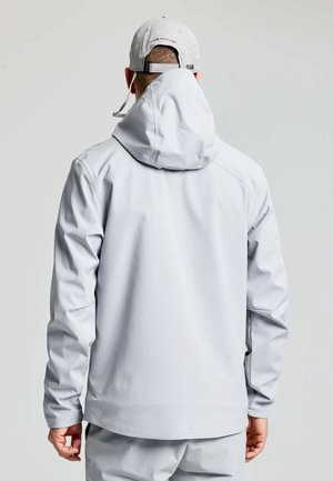 Lichtgrijze waterdichte jas met een capuchon, voorzien van elastische manchetten, een gladde textuur en een relaxte pasvorm. De achterkant toont minimale detailing.