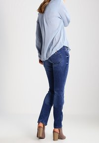 Blusa de manga larga azul clara con diseño de espalda partida, combinada con jeans ajustados azul oscuro y botas de tobillo topo con tacón apilado.