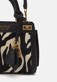 Bolso de mano con estampado de cebra en blanco y negro, con detalles en dorado, ribetes de cuero y un pequeño pouch desmontable; diseño estructurado.