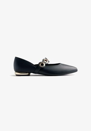 Scarpa piatta nera in pelle con punta appuntita, due grandi fibbie circolari dorate sulla cinghia e un piccolo tacco con accenti dorati.