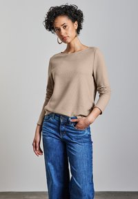 Beige långärmad topp i ett mjukt material, tillsammans med löst sittande blå denimjeans. Har en vid halsringning och en avslappnad passform.