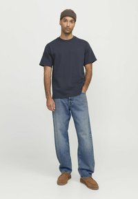 Navyblaue Baumwoll-T-Shirt mit lockerem Schnitt, kombiniert mit hellen, gewaschenen Denim-Jeans und braunen Wildleder-Slippern. Einfaches, minimalistisches Design.