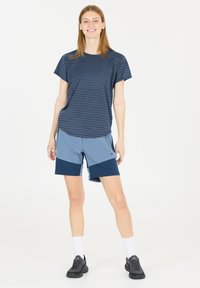 Musta raidallinen lyhythihainen paita yhdistettynä vaaleansinisiin ja tummansinisiin väri-blokattuihin shortseihin. Paidan kanssa valkoiset nilkkasukat ja mustat urheilukengät.