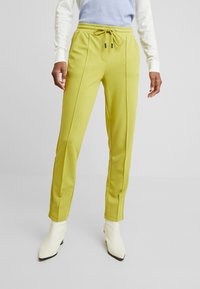 Lime green jogger pants with a drawstring waist, sleek design, and subtle vertical seam details, paired with white pointed ankle boots.