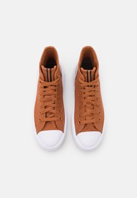 Wysokie trampki z brązową płócienną cholewką, białą gumową podeszwą i zaokrąglonym noskiem. Posiadają sznurowadła i czarne paski ozdobne wokół kostki.