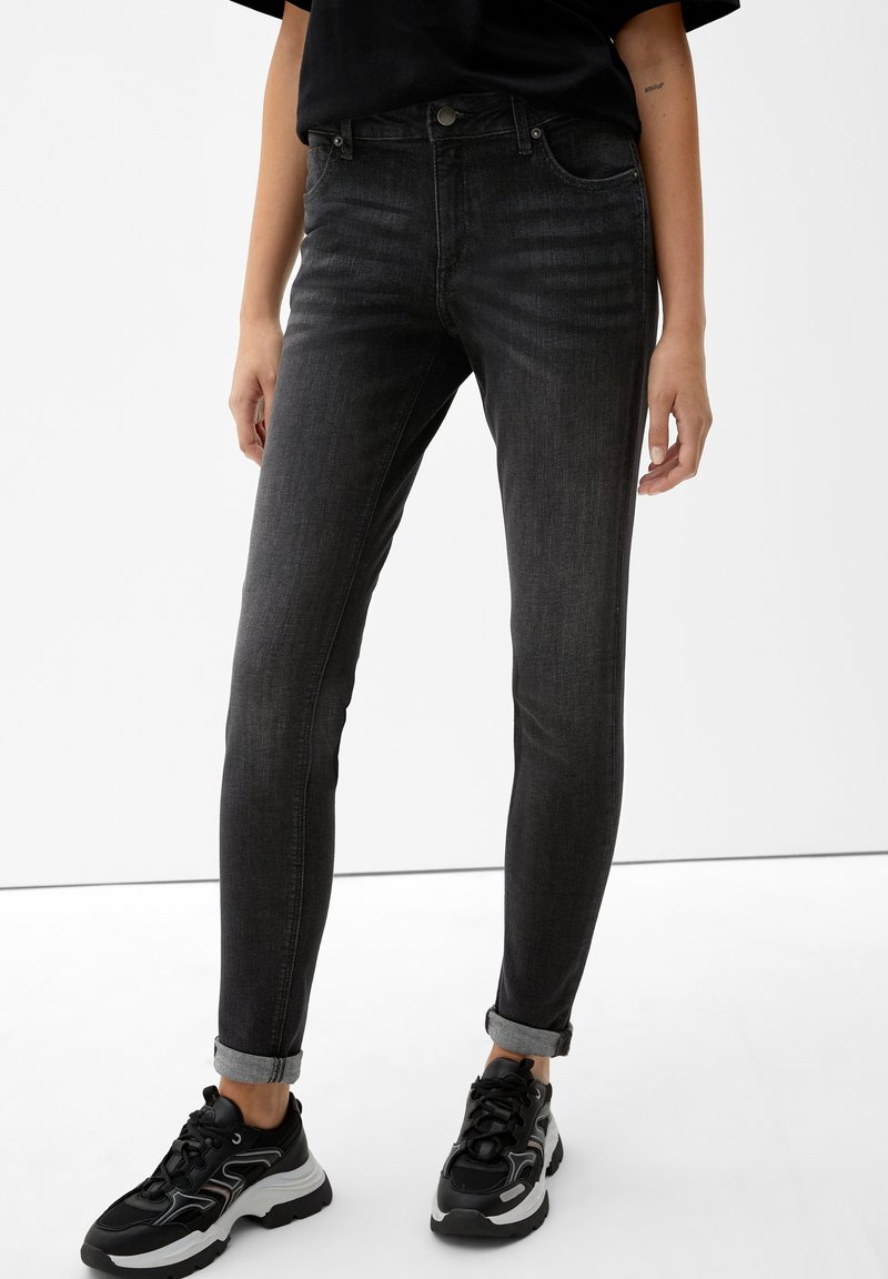 Črne skinny jeans z visokim pasom, z rahlim bledenjem, petimi žepi in z zavihanimi robovi, v kombinaciji z črnimi in sivimi športnimi copati.
