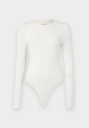 Biały bodysuit z długim rękawem wykonany z gładkiego materiału. Posiada okrągły dekolt i wysokie wycięcie na dole. Logo "Guess Jeans" w tłoczonym tekście.
