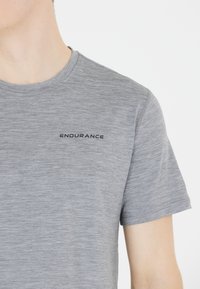 Graues T-Shirt mit kurzen Ärmeln und melierter Textur, Rundhalsausschnitt, mit einem schwarzen "ENDURANCE"-Logo auf der linken Brustseite.