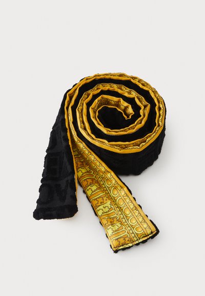 Material textil cu model negru și galben rulat în spirală, afișând un design decorativ cu margine aurie-galbenă pe o margine.