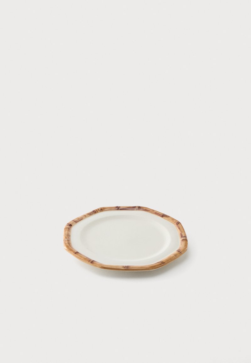 Assiette ovale en céramique blanche avec un bord texturé brun clair style bambou sur un fond clair uni.