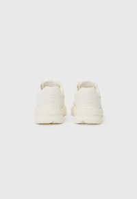White sneakers with a smooth matte finish, rounded shape, padded ankle support, subtle branding on the heel, and textured rubber sole.