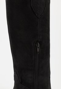 Bota alta de ante negra con cierre lateral y panel texturizado, acabado suave y una silueta elegante.