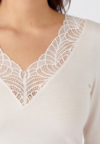 Lichtbeige lange mouwen top met een V-halslijn, versierd met ingewikkelde witte kantdetails, met een gladde textuur en een aansluitend ontwerp.