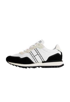 Zapatilla deportiva blanca y negra con parte superior de malla, acentos de ante texturizado, rayas contrastantes y suela de goma negra diseñada para tracción.