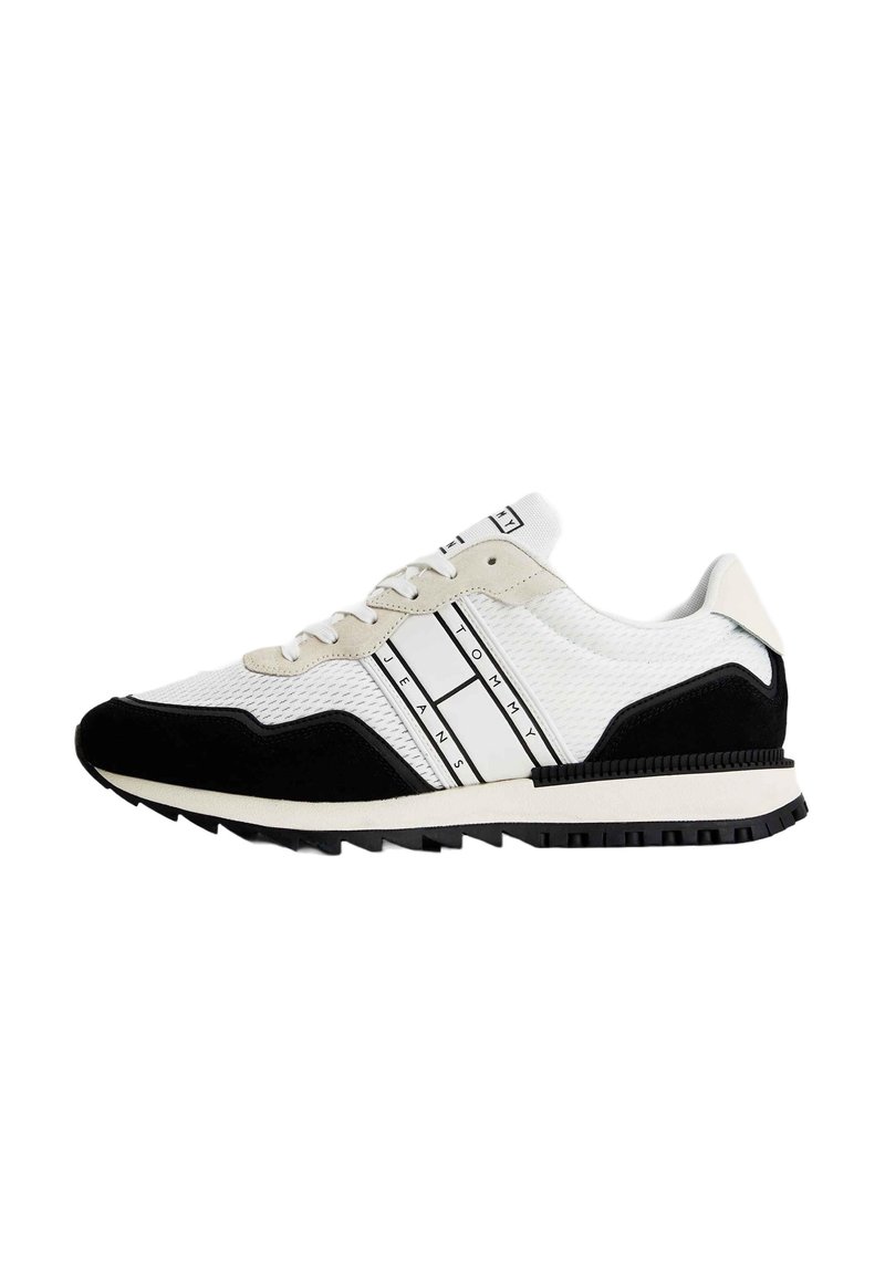 Zapatilla deportiva blanca y negra con parte superior de malla, acentos de ante texturizado, rayas contrastantes y suela de goma negra diseñada para tracción.