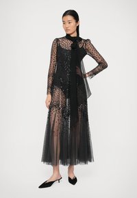 Must must värvitud kleit pikkade varrukatega, kaunistatud sädelevate litritega ja kaelal sidumisega. Omab voolavat tülliseelikut ja vormitut bodi.