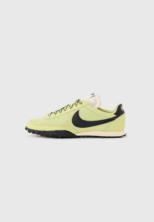 Chaussure de course Nike vert clair avec le logo Swoosh noir, lacets noirs et blancs, et semelle texturée sur un fond uni.
