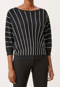Czarny sweter w paski z białymi pionowymi liniami, dekolt łódka, rękawy 3/4 oraz ribbowany dół. Wykonany z teksturowanej, miękkiej tkaniny.