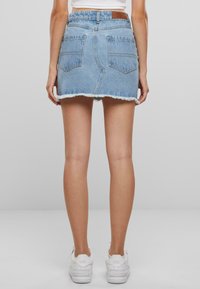 Lyseblå denim mini-skjørt med frynset nederkant, to lommer bak, og en brun lærmerke på livbåndet. Stylet med hvite joggesko.