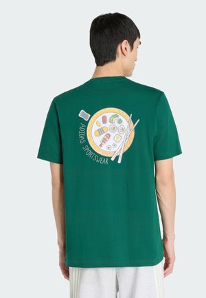 Homme portant un T-shirt vert Adidas avec une assiette de sushi, des baguettes et le texte « ADIDAS SPORTSWEAR » dans le dos, vu de dos.