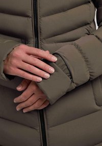 Giacca imbottita verde oliva con una tasca con zip sulla manica e una zip prominente sul davanti, che mostra un design elegante.