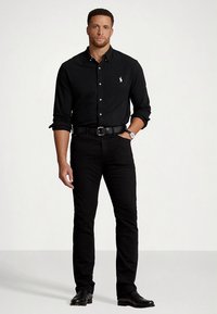 Juoda marškinėliai, užsegami mygtukais, su polo logotipu, derinami su juodais džinsais, juodu diržu ir oficialia avalyne. Lygus audinys su glaustais siūlais.