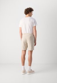 Shorts beige en tissu texturé, avec une taille élastique et une poche arrière. Assortis à un t-shirt blanc et des chaussures légères.