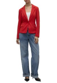 Veste cintrée rouge avec revers, deux poches devant, associée à un jeans large bleu clair. Des escarpins noirs à bout pointu complètent la tenue.