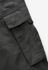 Dunkelgrauer, strukturierter Stoff mit gesteppten Akzenten und einer Klappentasche. Das Material wirkt strapazierfähig und ist für legere oder Outdoor-Nutzung geeignet.
