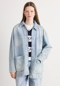 Veste en denim bleu clair avec une coupe décontractée, comportant deux poches avant, un col pointu et des fermetures bouton à l'avant.